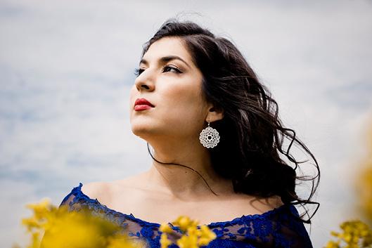 A women with dark browb wavy hair wearing a mandala wearing and a navy blue lace top